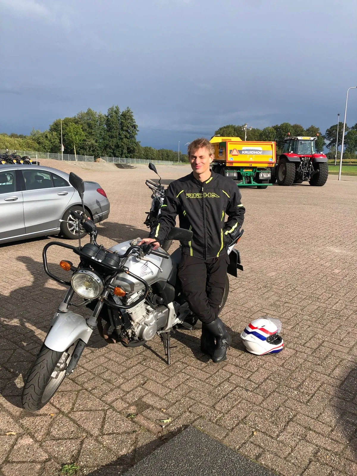 Leerling in motorkleding leunt tegen een lesmotor op het oefenterrein
